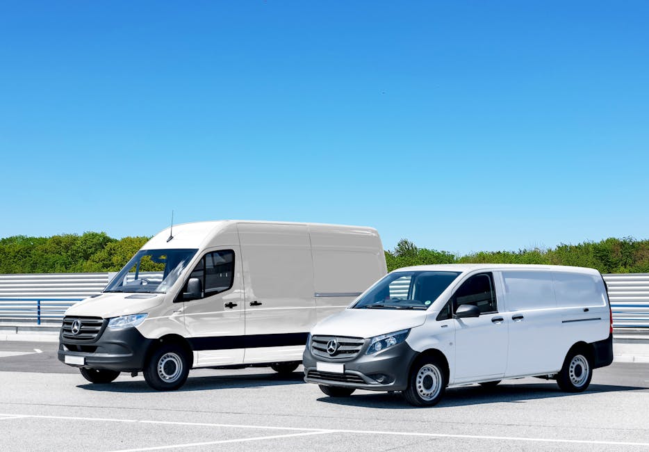 A white commercial van parked on a street next to a building with a large glass window and a white wall. The van's rear door is slightly open, revealing a clean, organized interior. Outside, three large blue plastic bags filled with cleaning supplies or waste are placed on the pavement near the back of the van. The pavement is smooth, and the scene is illuminated by natural daylight, highlighting the clean and well-maintained condition of the van and surroundings. This image exemplifies exterior commercial vehicle logistics related to surface cleaning and hygiene services, aligning with Kennington Cleaners' emphasis on professional cleaning and sanitisation, as referenced in the Kennington council permit guide for commercial cleaning vans.